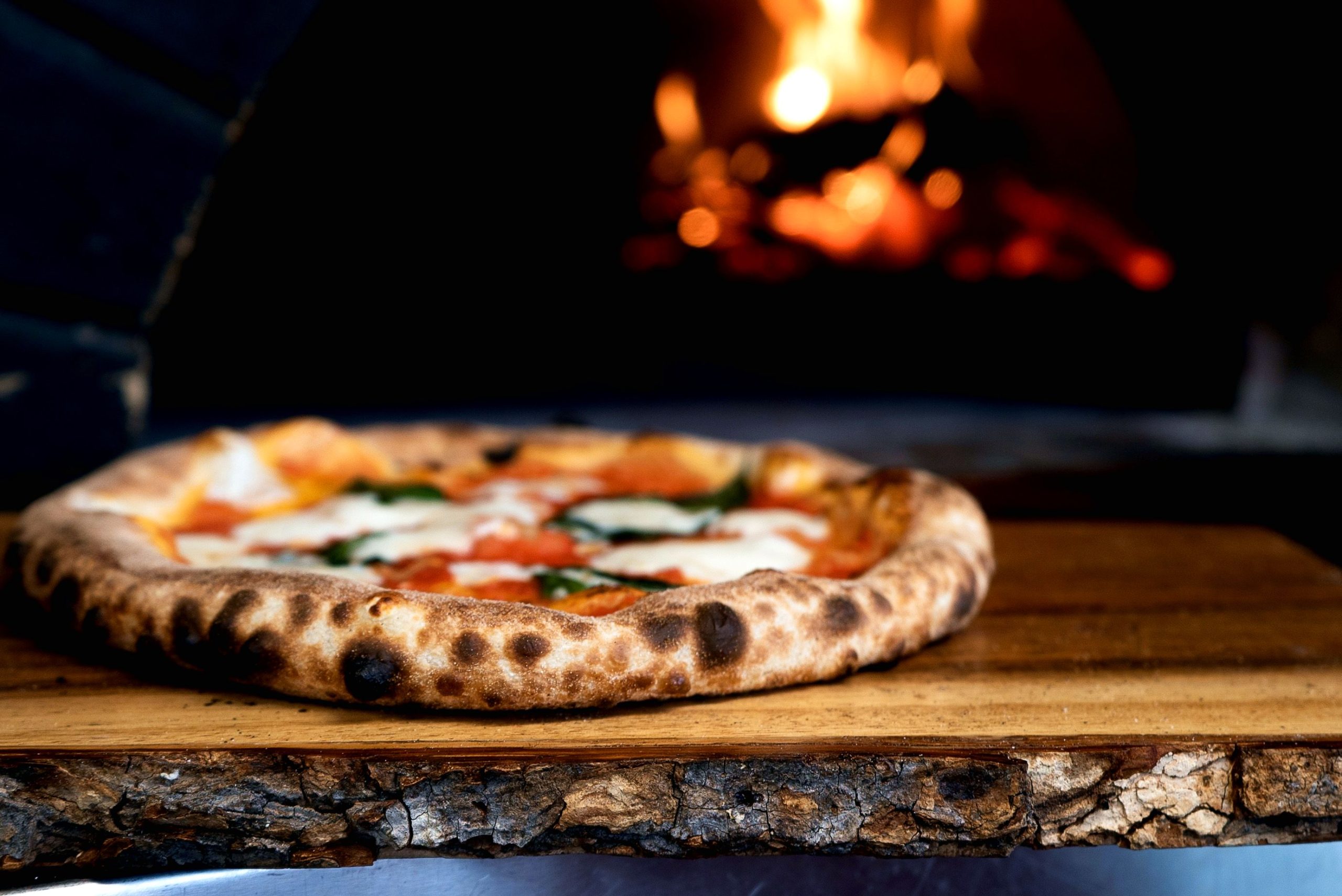 A photo of a pizza in front of a wood-fired oven.